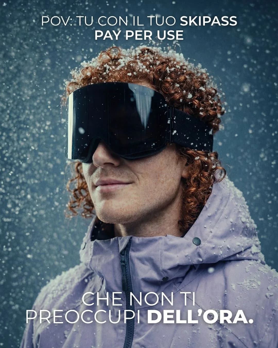 Ritratto ravvicinato di uno snowboarder con maschera scura e riccioli rossi, sotto la neve che cade