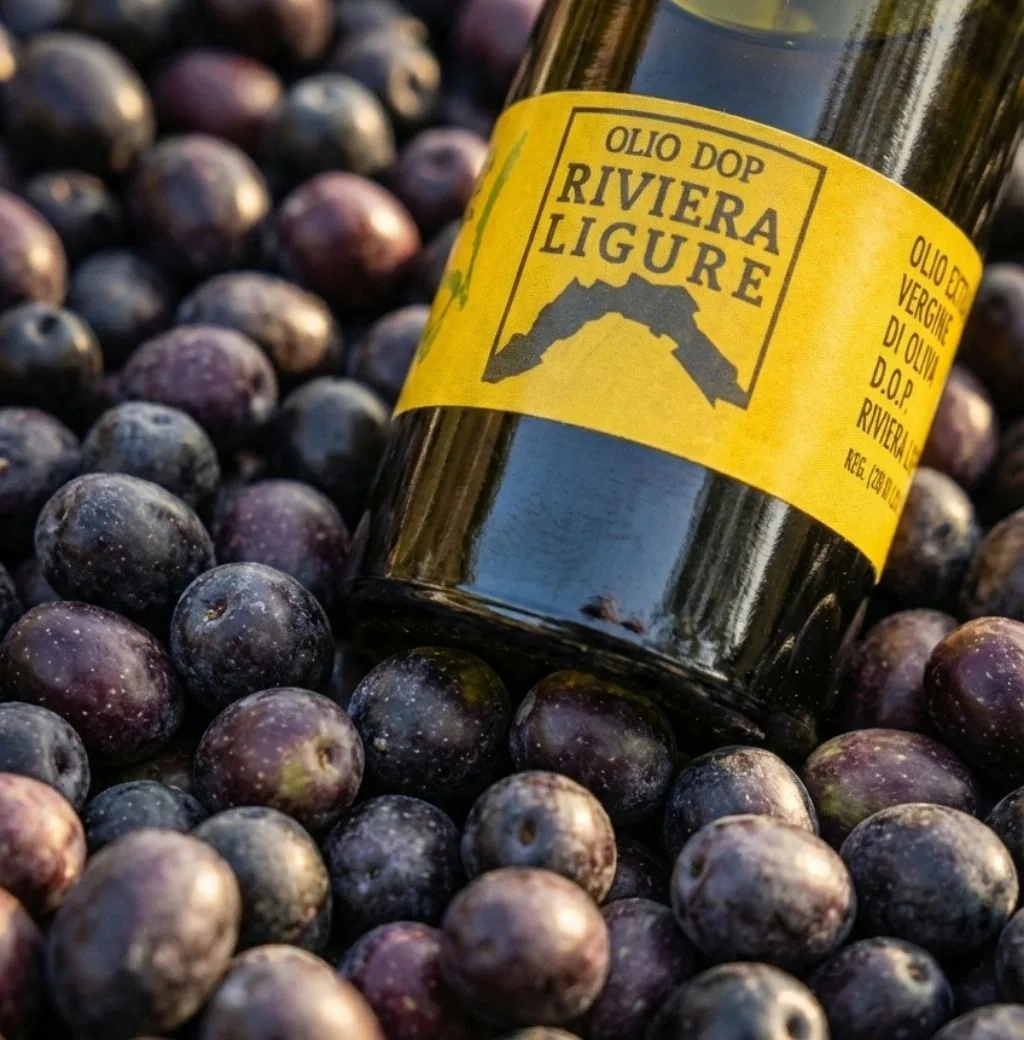 Bottiglia di olio DOP Riviera Ligure con l'etichetta gialla, appoggiata su un letto di olive nere